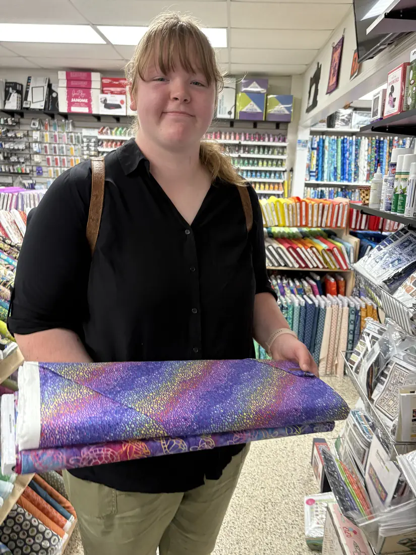 Abigail at a fabric shop, holding bolts of fabric