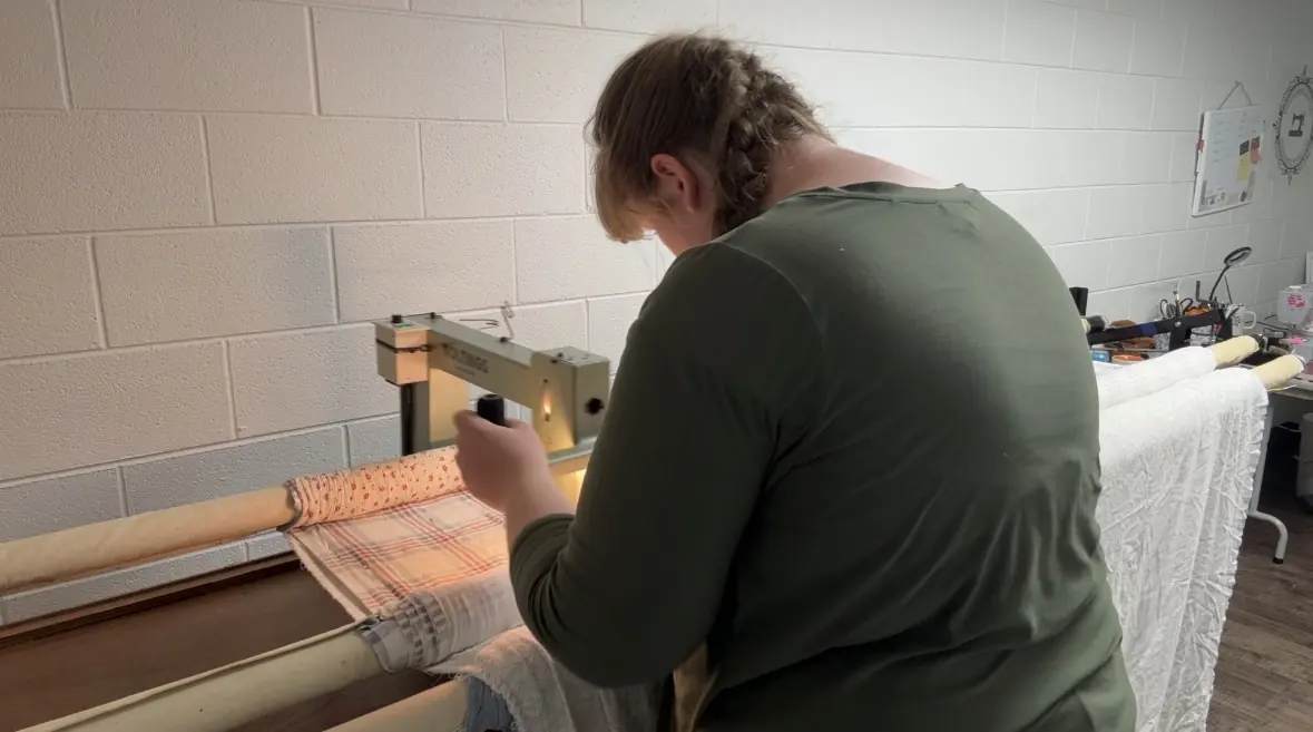 Abigail guiding the long-arm machine by hand across a quilt